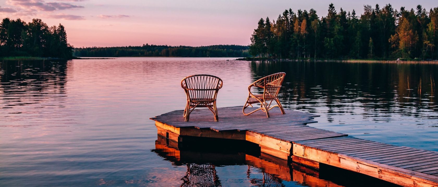 Kaksi tuolia laiturilla tyynen järven rannalla. taivas on värjäytynyt auringonlaskun väreihin.